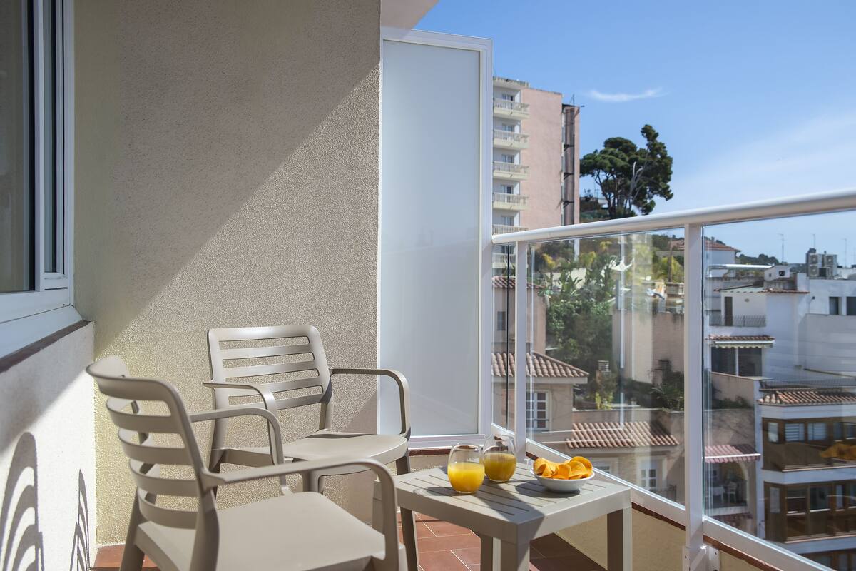 A balcony with a table and chairs, a glass door, and a view of buildings and trees.
