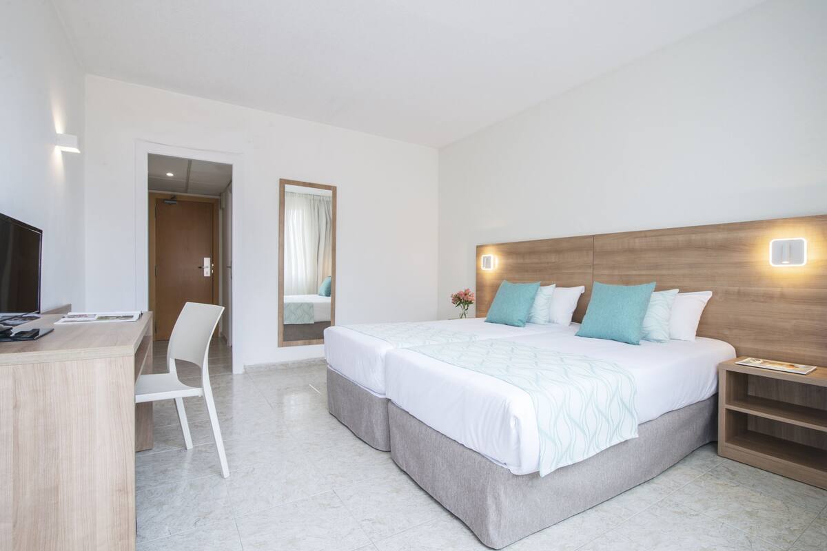 A hotel room with a bed, bedside table, chair, desk, and a mirror.
