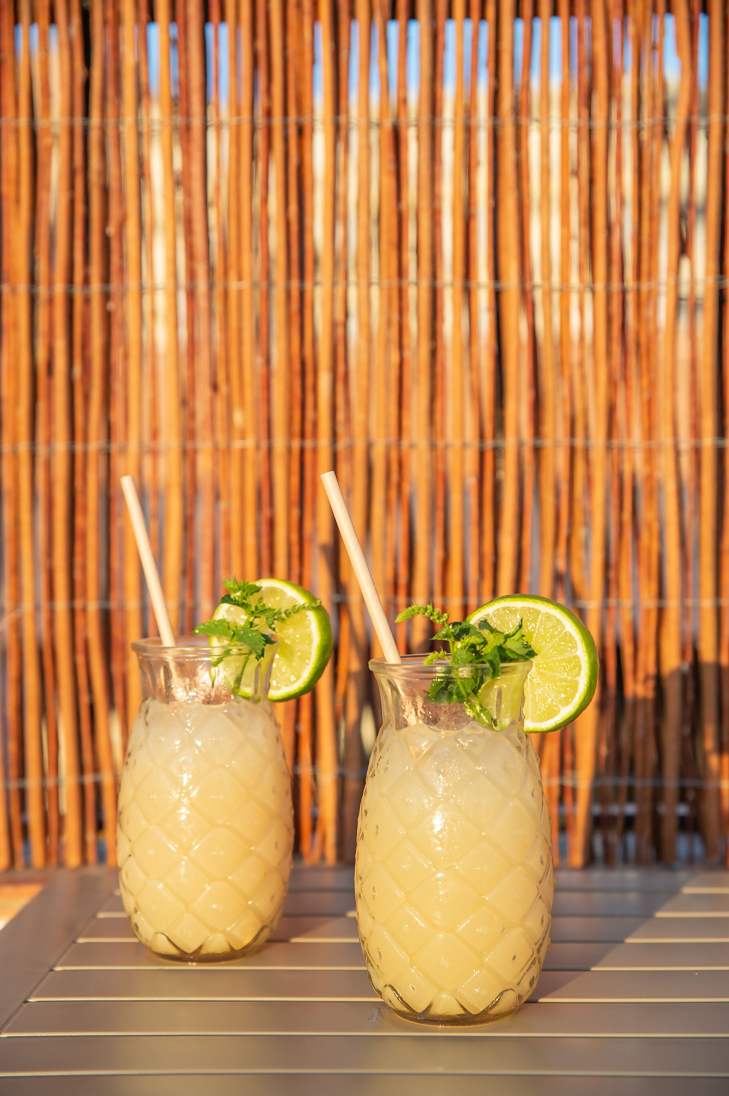 Two glass pitchers with lime slices and mint on a table with a bamboo backdrop.