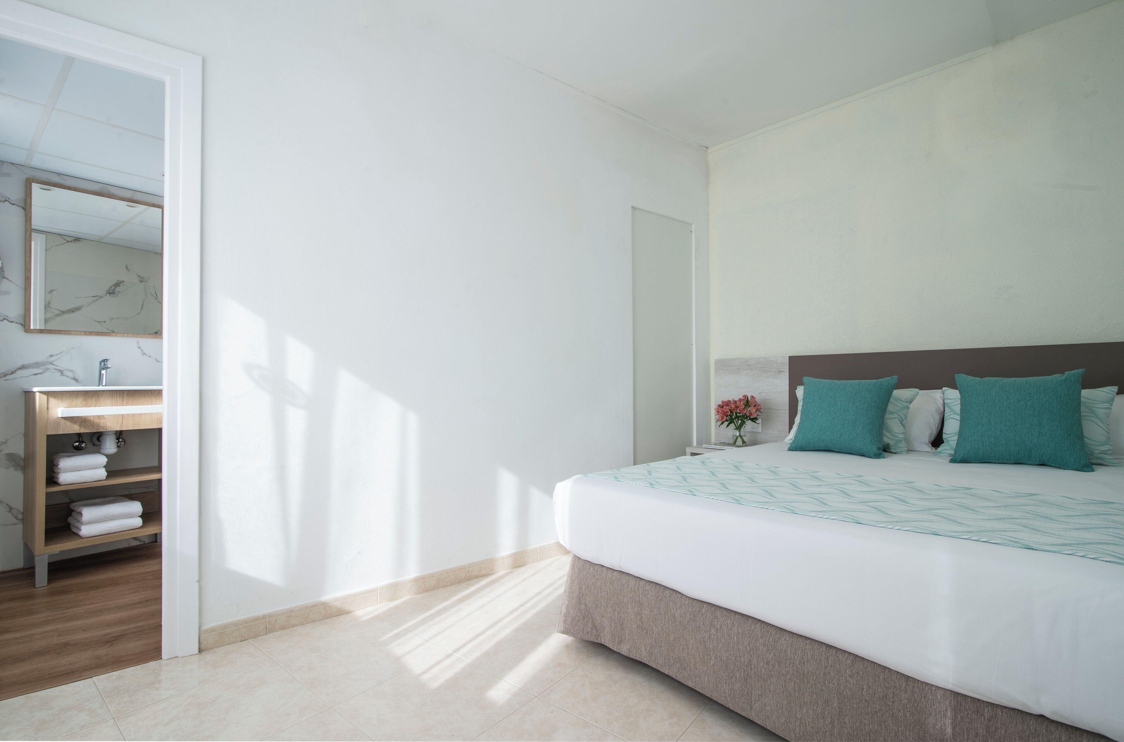 A bedroom with a bed, a nightstand, a mirror, and a wooden shelf with towels.