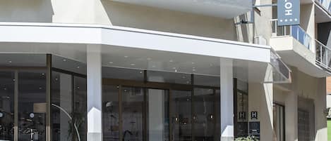 A modern hotel entrance with a glass facade, a covered entrance area, and a visible staircase leading to the entrance.