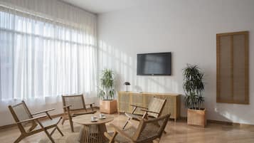 A modern living room with a round coffee table, wicker chairs, a TV mounted on the wall, and two potted plants.