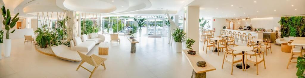 Un hall d’hôtel moderne doté d’espaces aménagés avec des sièges, d’un bar et de plantes d’intérieur.