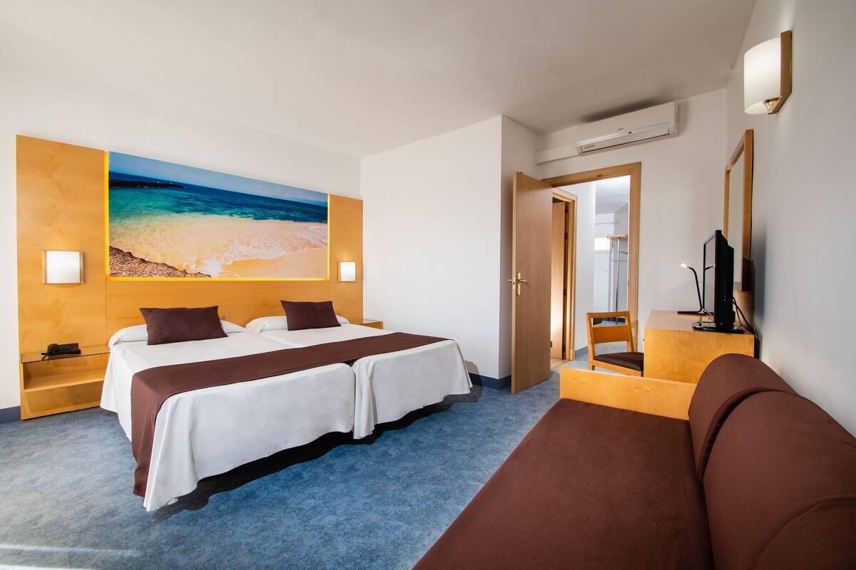 Une chambre d’hôtel avec un lit, une télévision, un bureau et un grand tableau représentant une plage accroché au mur.