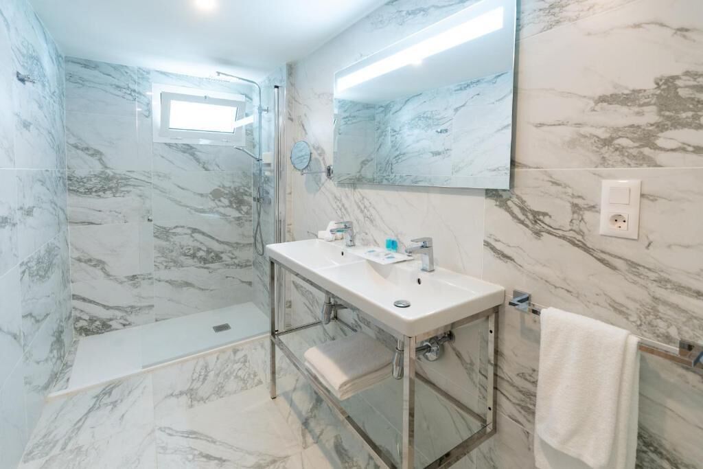 Un baño con cabina de ducha de vidrio, un lavabo blanco y un espejo grande.