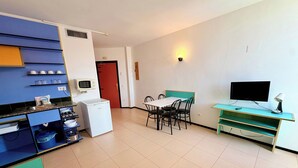Un espacio habitable compacto con kitchenette, comedor, televisor y refrigerador pequeño.