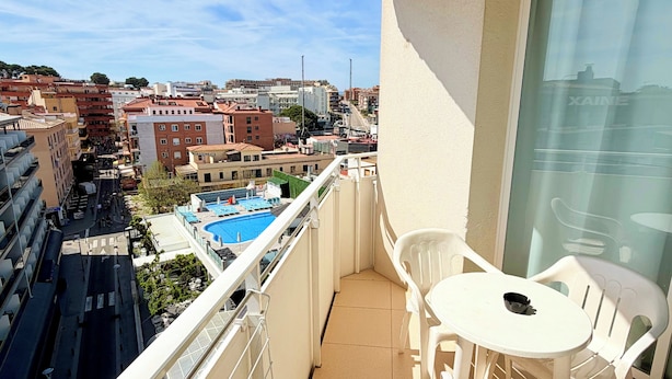 Un balcón con vista a un paisaje urbano, una piscina y sillas de plástico blanco.