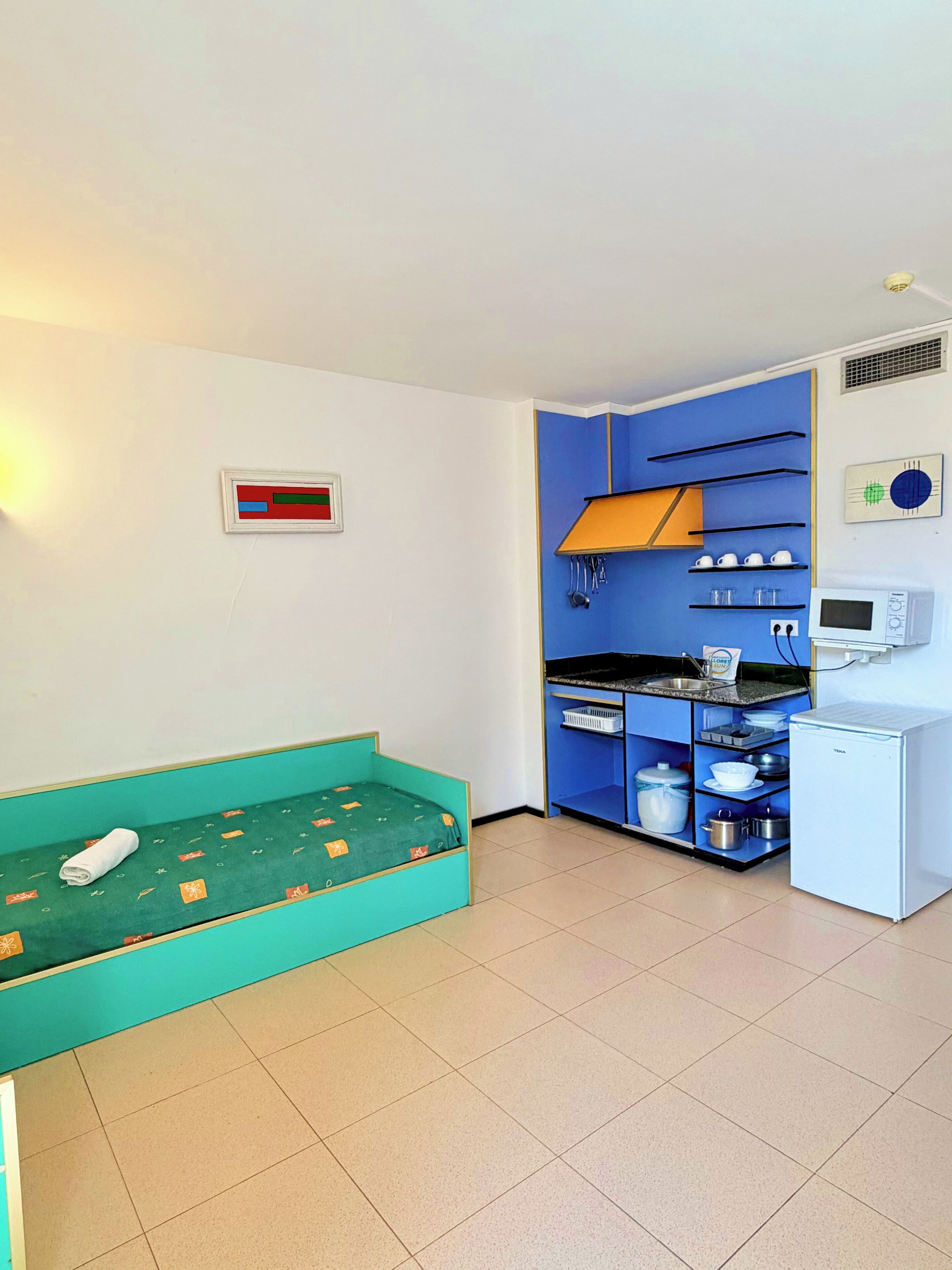 Ein kleines Zimmer mit Bett, Küchenzeile und kleinem Kühlschrank.