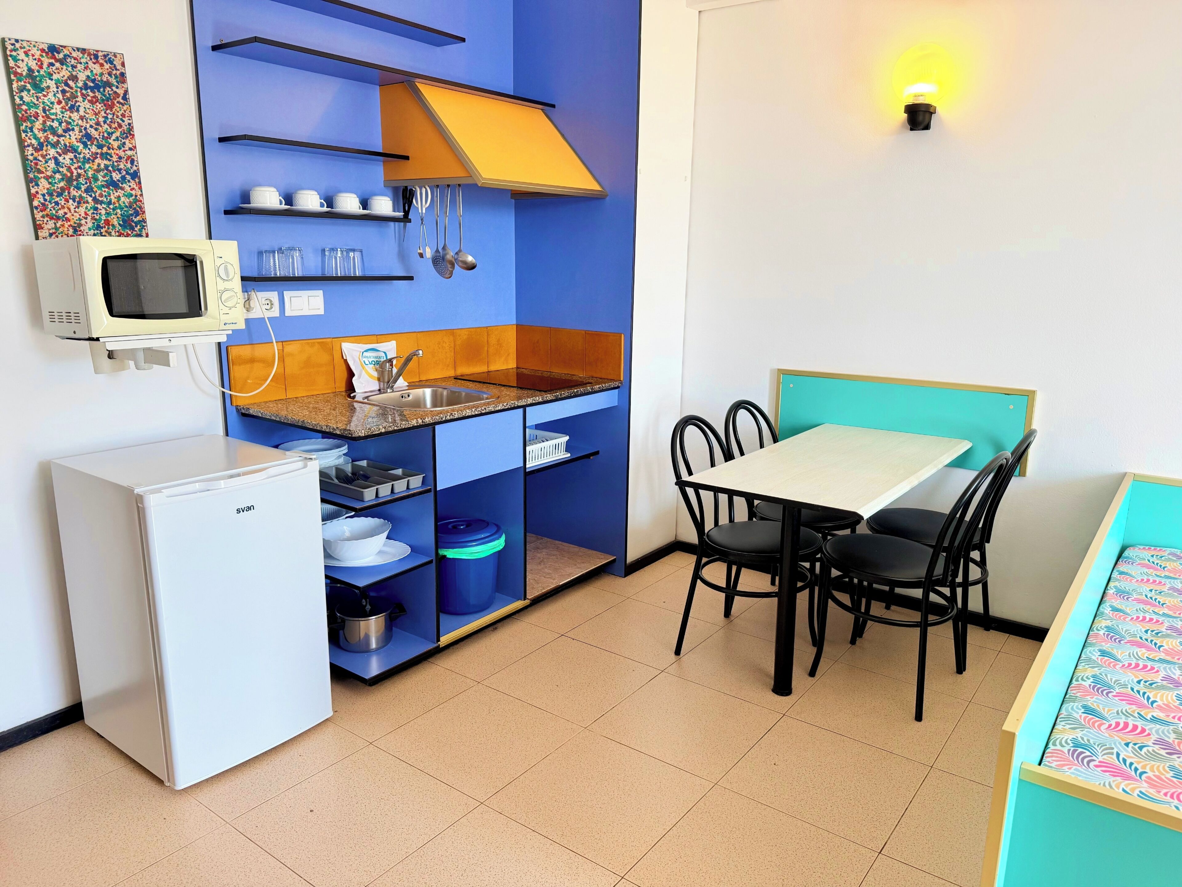 A compact kitchenette with a microwave, sink, and storage shelves. There is a dining area with a table and chairs.