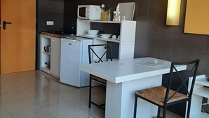 Una cocina moderna con armarios blancos, un microondas y una estufa. Hay dos sillas con estructura negra y cojines marrones. El piso está cubierto de baldosas y las paredes son oscuras.