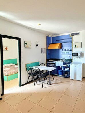 A compact room with a dining table, chairs, a kitchenette, and a bed with a green headboard. - Apartaments Lloret Sun (Lloret de Mar)