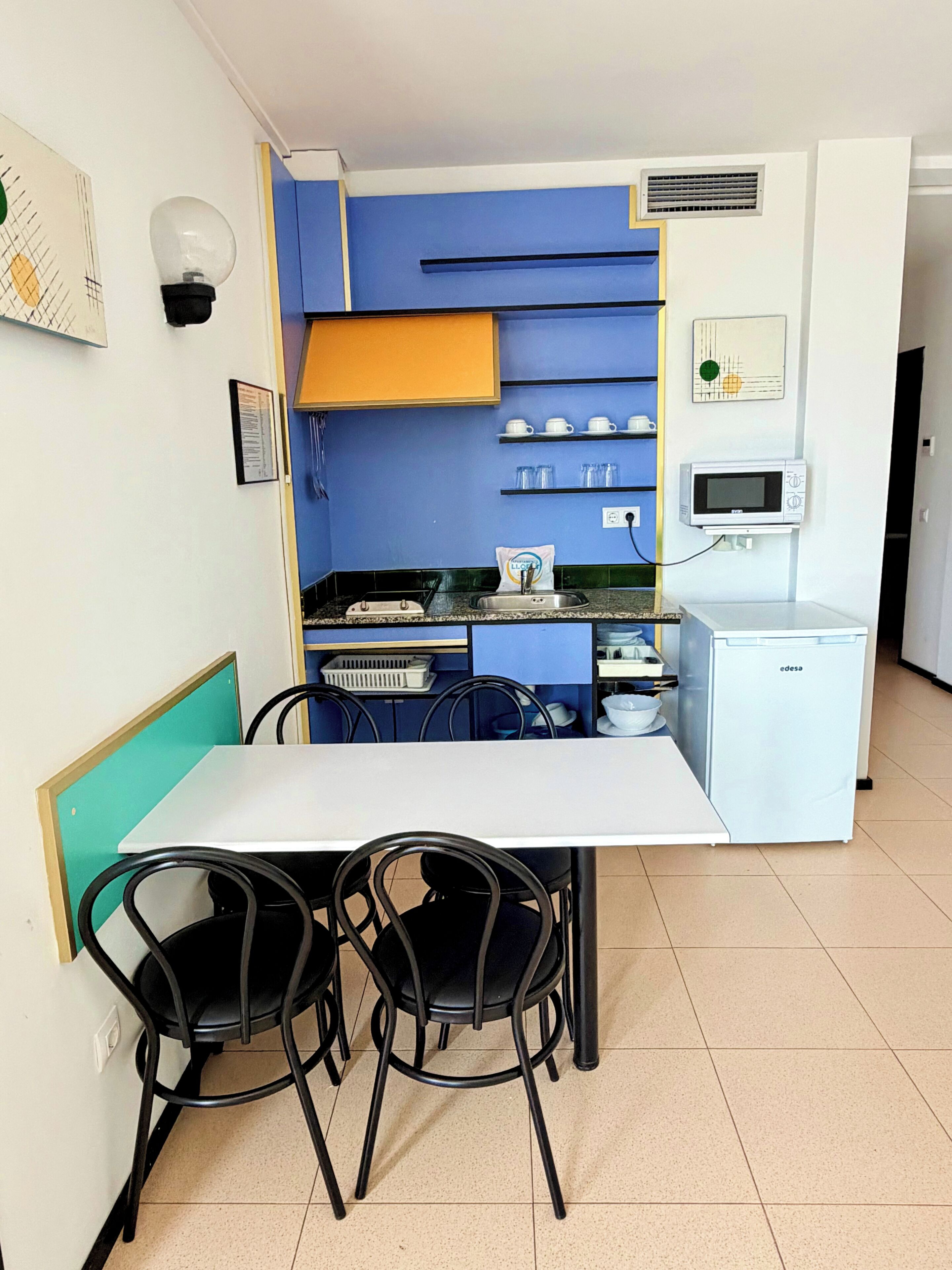 Una kitchenette compacta con microondas, un refrigerador pequeño y un lavamanos. Hay dos sillas y una mesa en la zona de comedor.