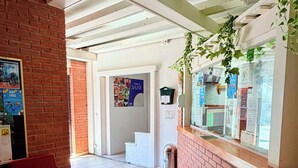 Un área de recepción con un banco rojo, un tablón de anuncios con varios avisos y una escalera que sube a otro piso.