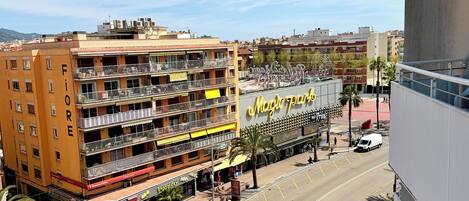 Un hotel de varios pisos con balcones, un restaurante a la vista y una calle con vehículos y peatones.