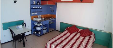 A compact bedroom with a bed, a small desk, and a kitchenette.