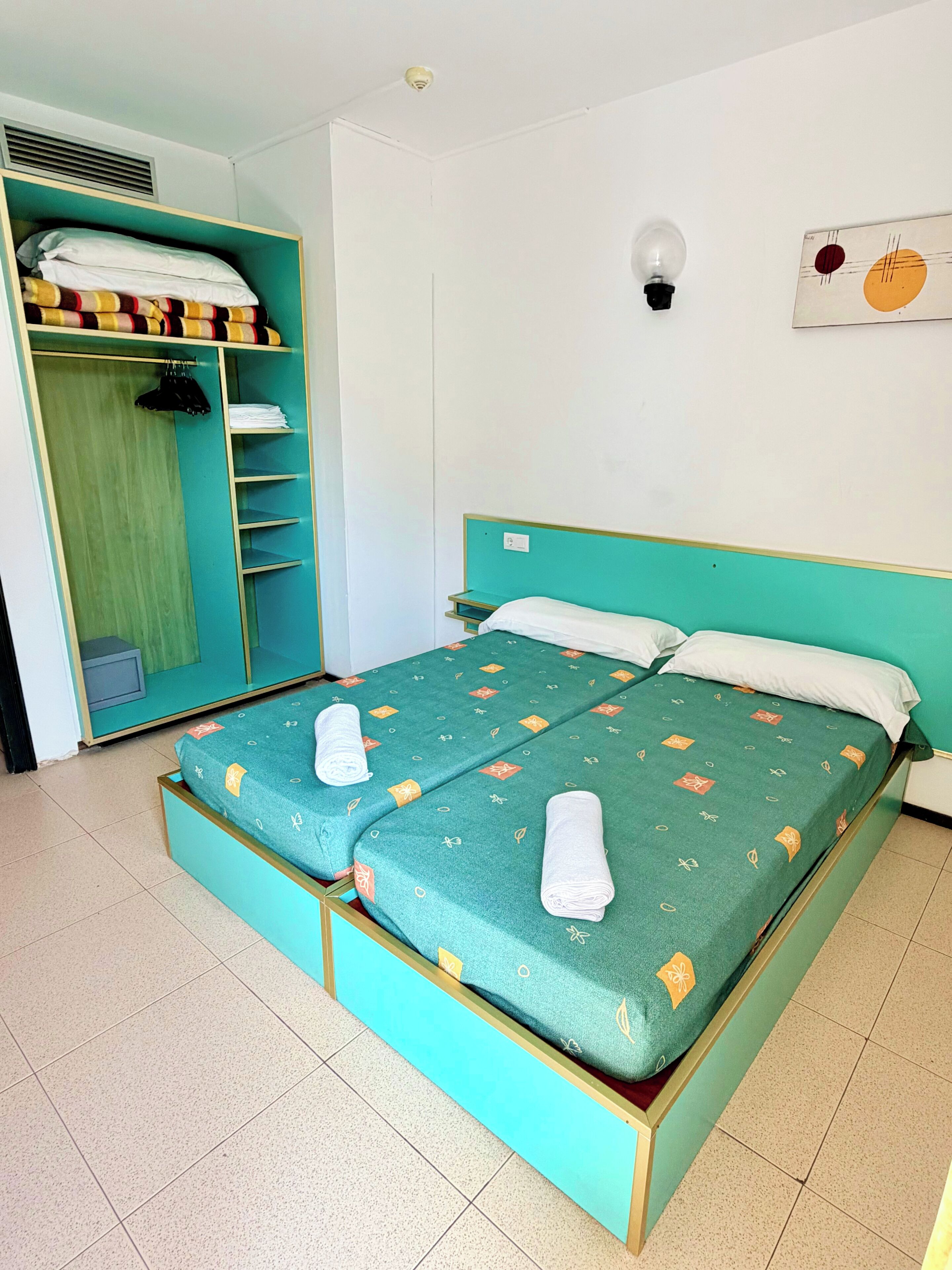 A twin bed with a teal headboard and footboard, two pillows, and a green bedspread with a pattern.