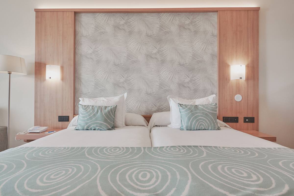 Un lit double avec une couvre-lit à motifs, deux oreillers, une tête de lit ornée d’un motif de feuilles et deux lampes de chevet.