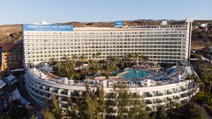A large hotel with a pool, multiple balconies, and a sign for 'GLORIA PALACE SAN AGUSTIN'.