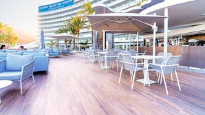 A cruise ship's outdoor dining area with seating and umbrellas, a bar, and a sign for Gloria Palace San Agustin.