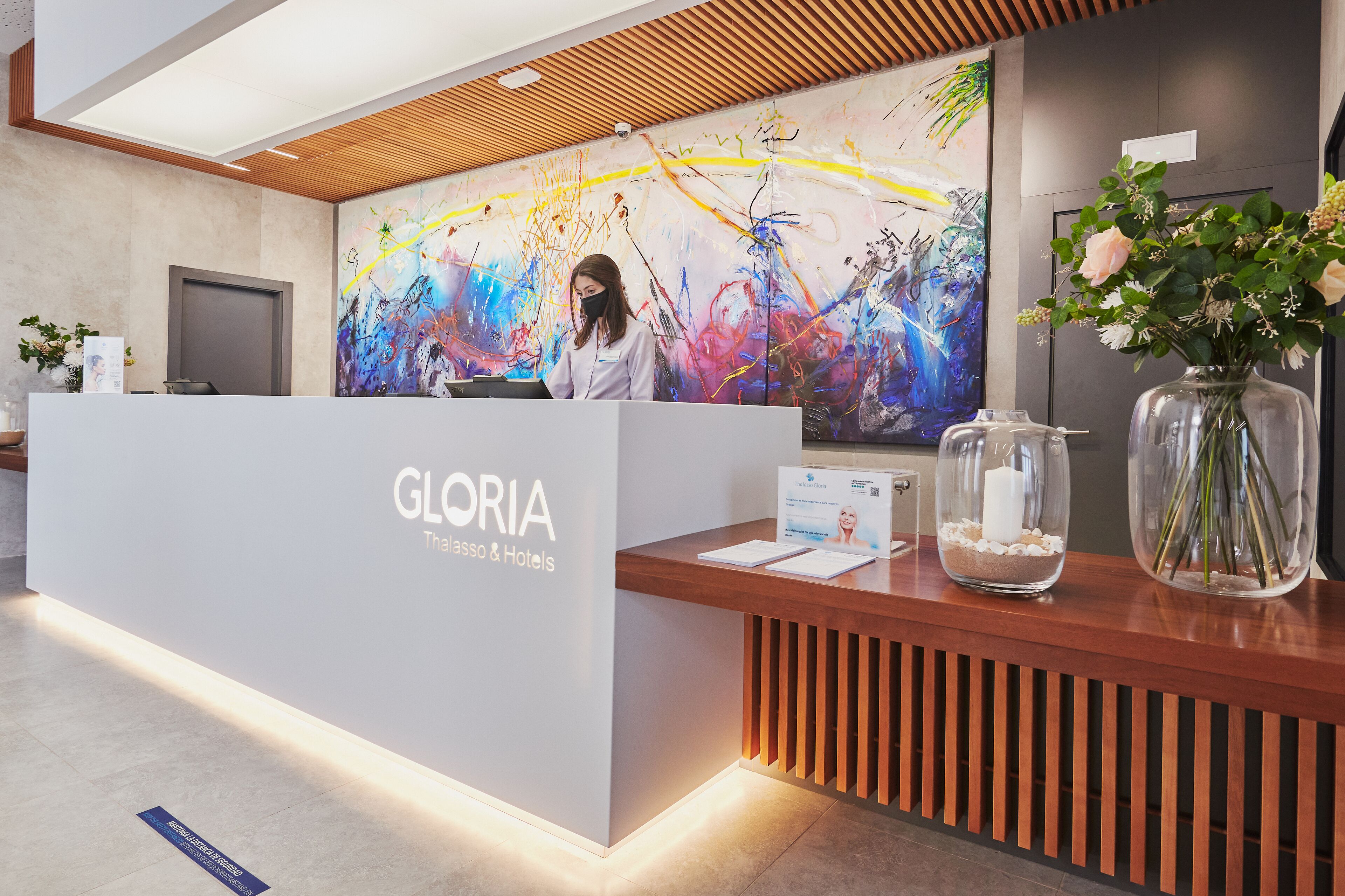 Un mostrador de recepción de diseño moderno, un cuadro abstracto grande y un jarrón con flores.