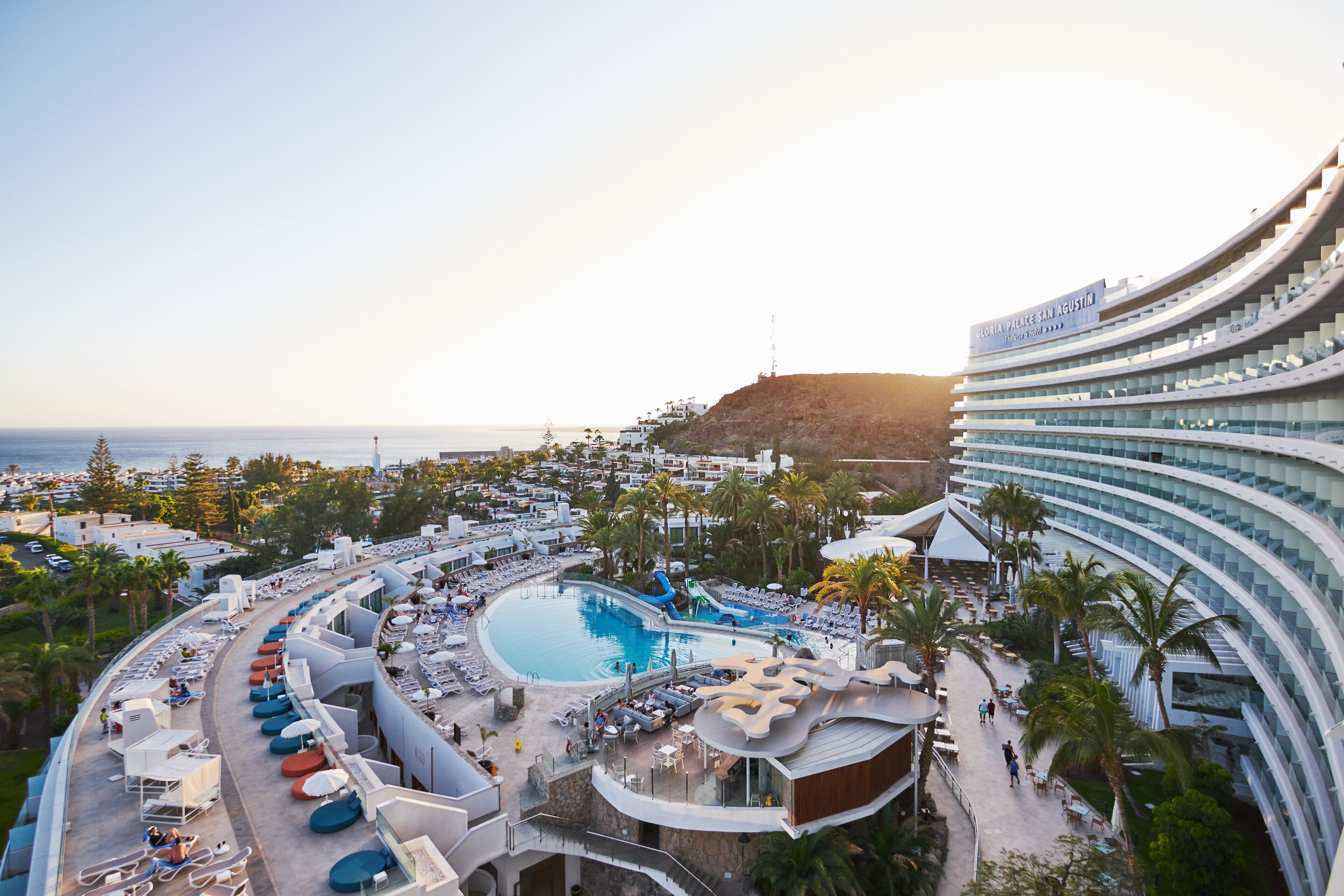 Un resort con una piscina grande, asientos al aire libre y vistas al mar.