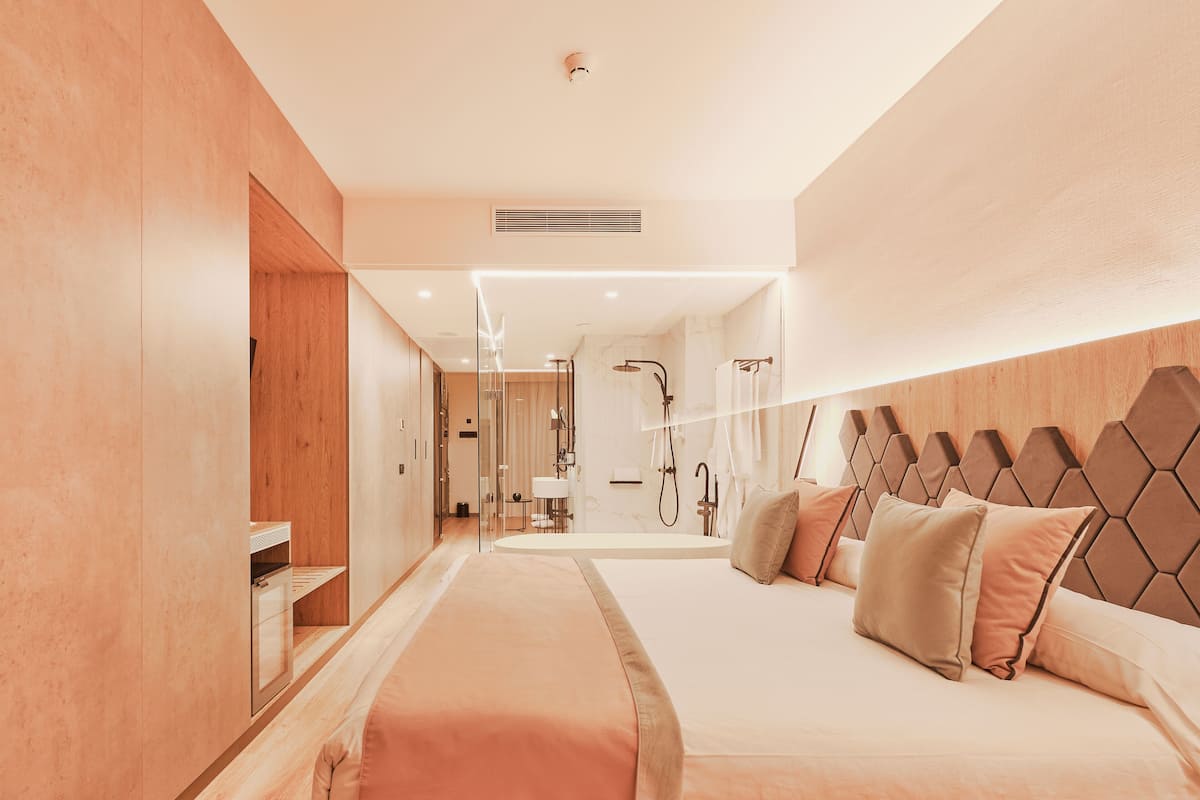 Une chambre d’hôtel moderne avec un grand lit, une tête de lit en bois et un dressing.