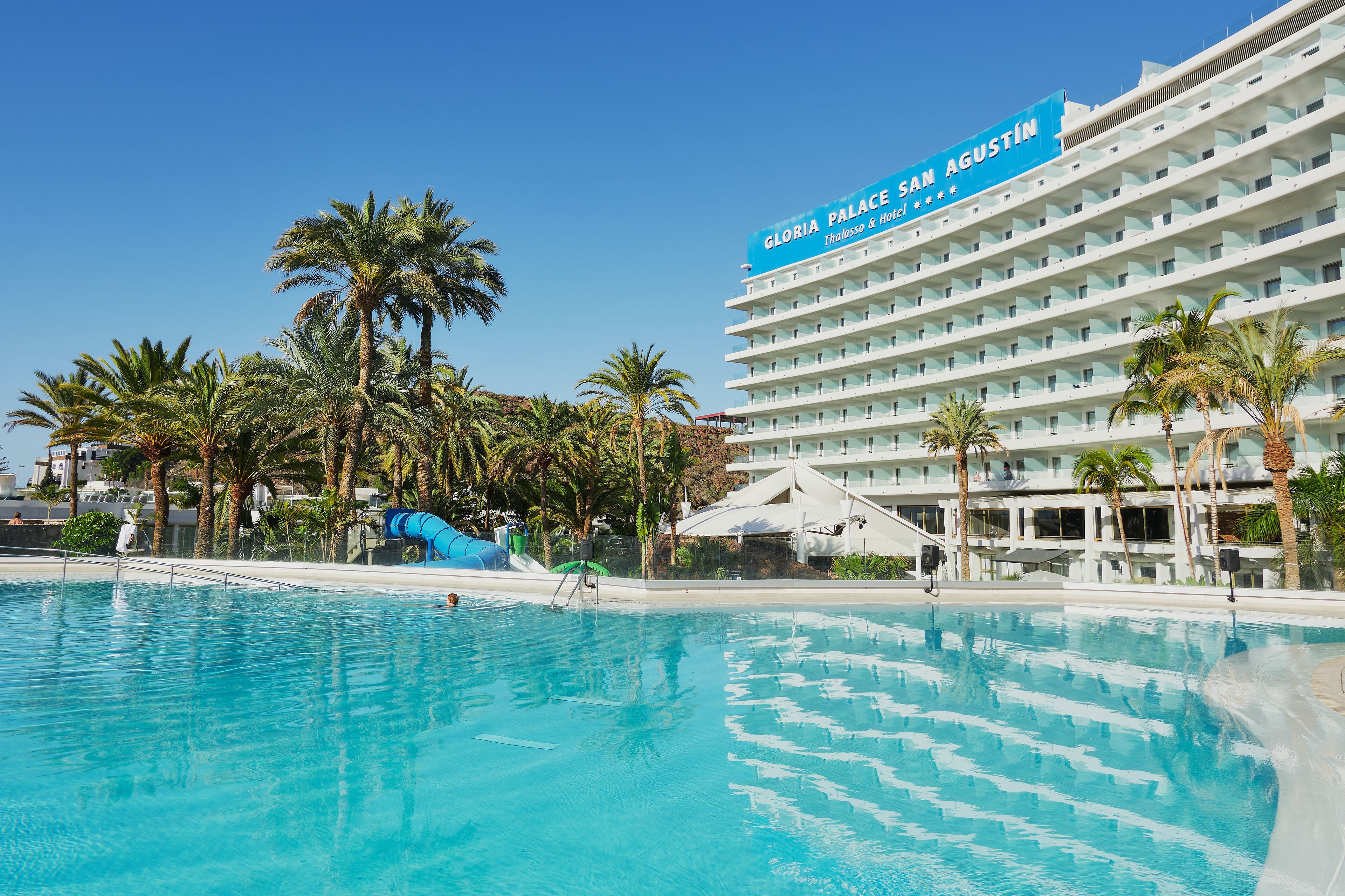 Un hotel con piscina, palmeras y un cartel que dice "Gloria Palace San Agustin".