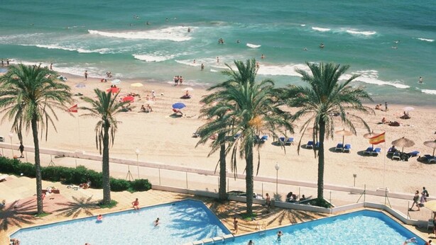 A beach resort with a swimming pool, palm trees, and beachgoers. - Aparthotel Londres (San Javier)