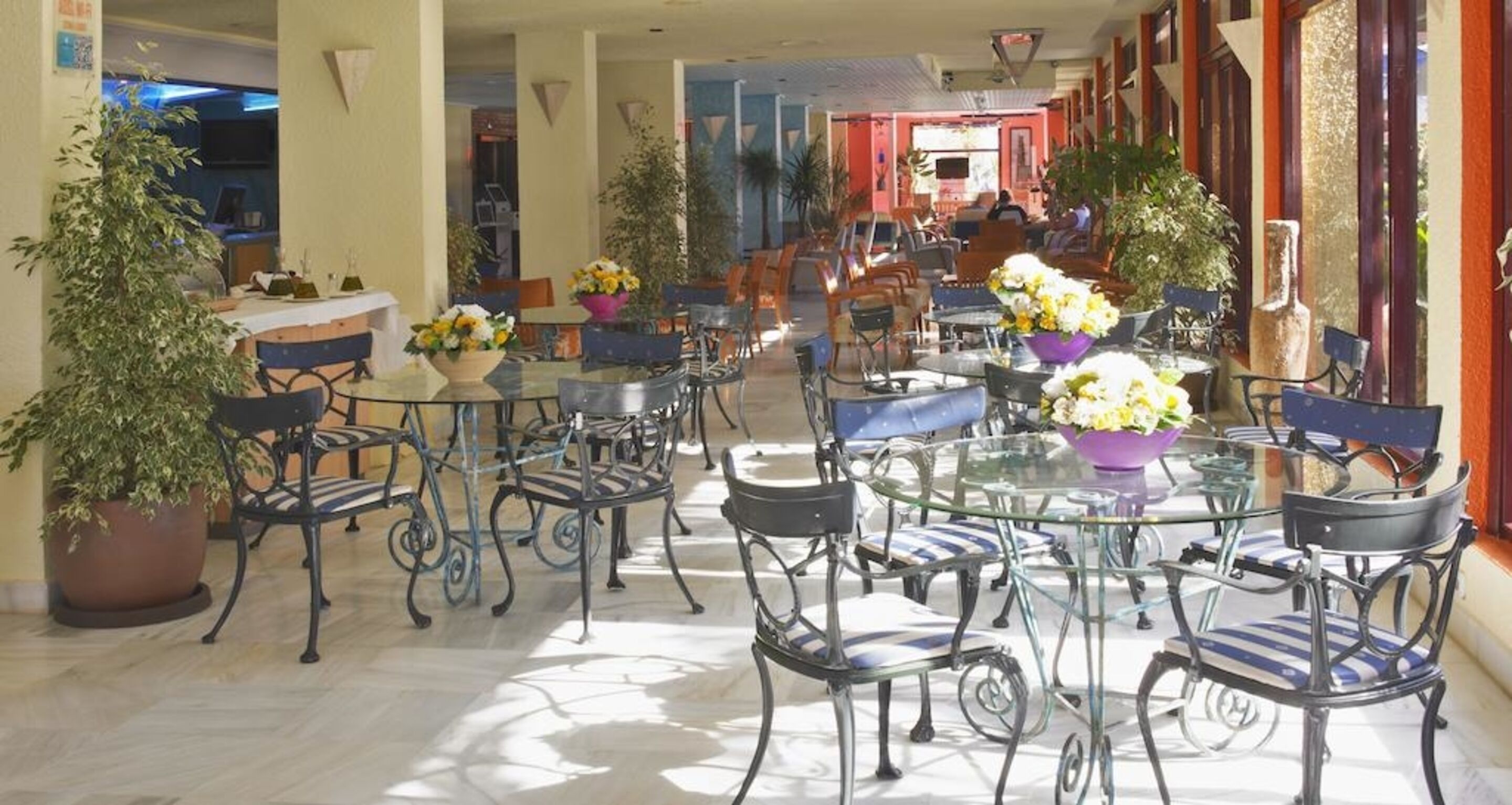 An indoor patio area with round tables and chairs, potted plants, and a view of the interior.