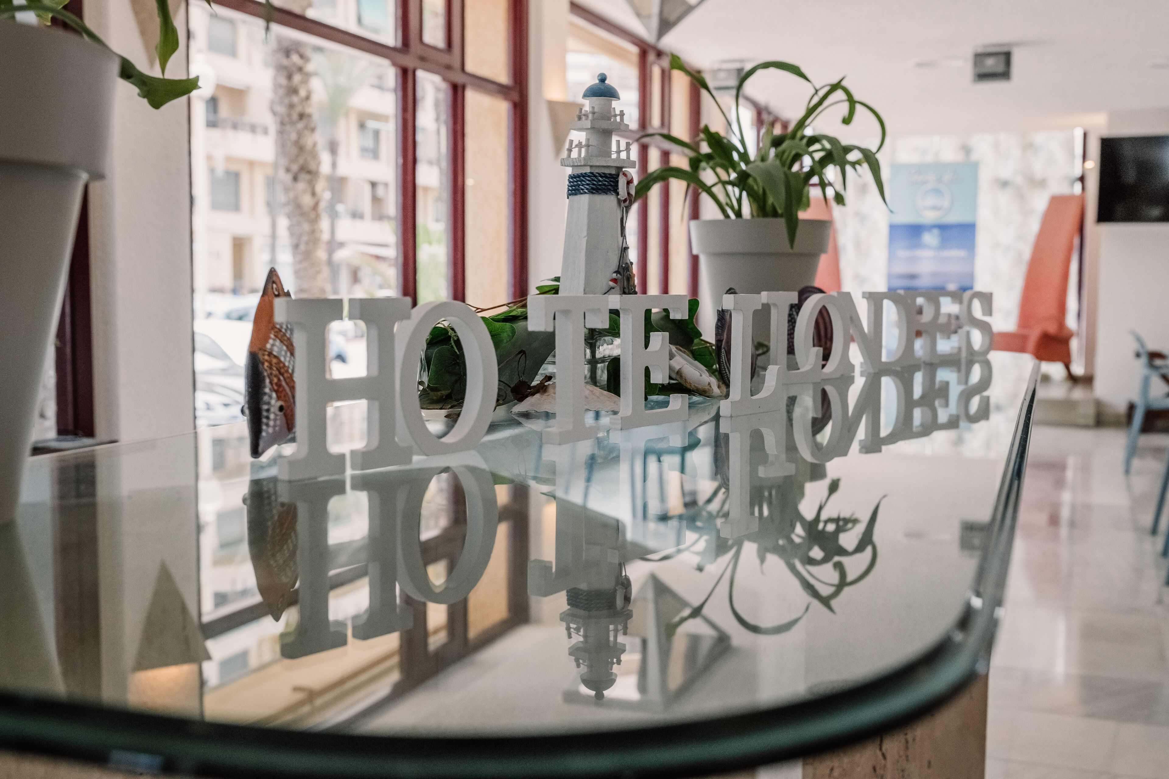 A reception desk with a glass top, a potted plant, and a decorative lighthouse model.