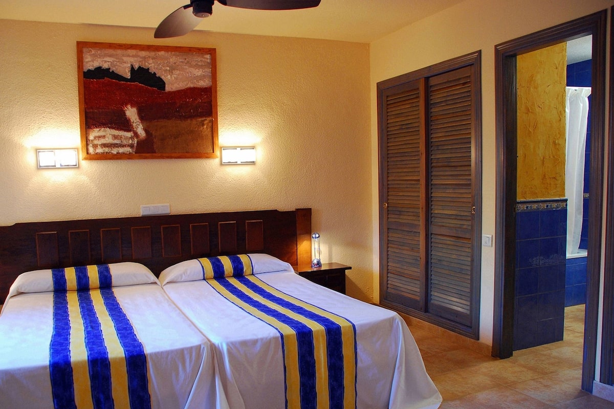 A hotel room with two beds, a painting on the wall, and a door leading to a balcony.