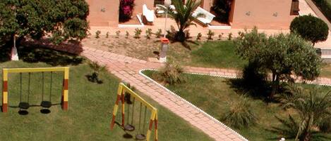 A courtyard with a swing set, a small red-roofed structure, and a pathway leading to a building entrance.