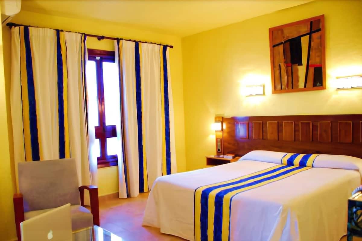 A hotel room with a bed, a chair, a nightstand, and curtains.