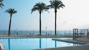 A swimming pool with palm trees and a view of the ocean. - Aparthotel Londres (San Javier)