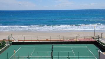 Una cancha de tenis con vista a la playa y al océano.