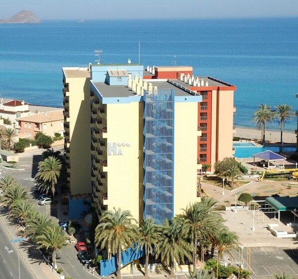 A multi-story hotel with a pool area and palm trees. - Aparthotel Londres (San Javier)