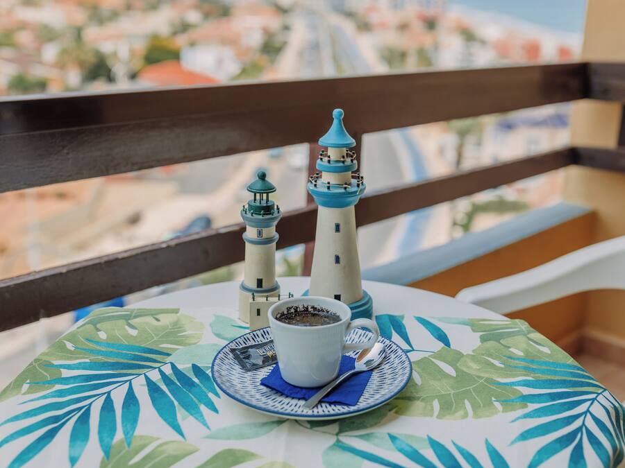 Una mesa con una taza de café, un plato y una cuchara sobre un mantel con estampado de hojas.