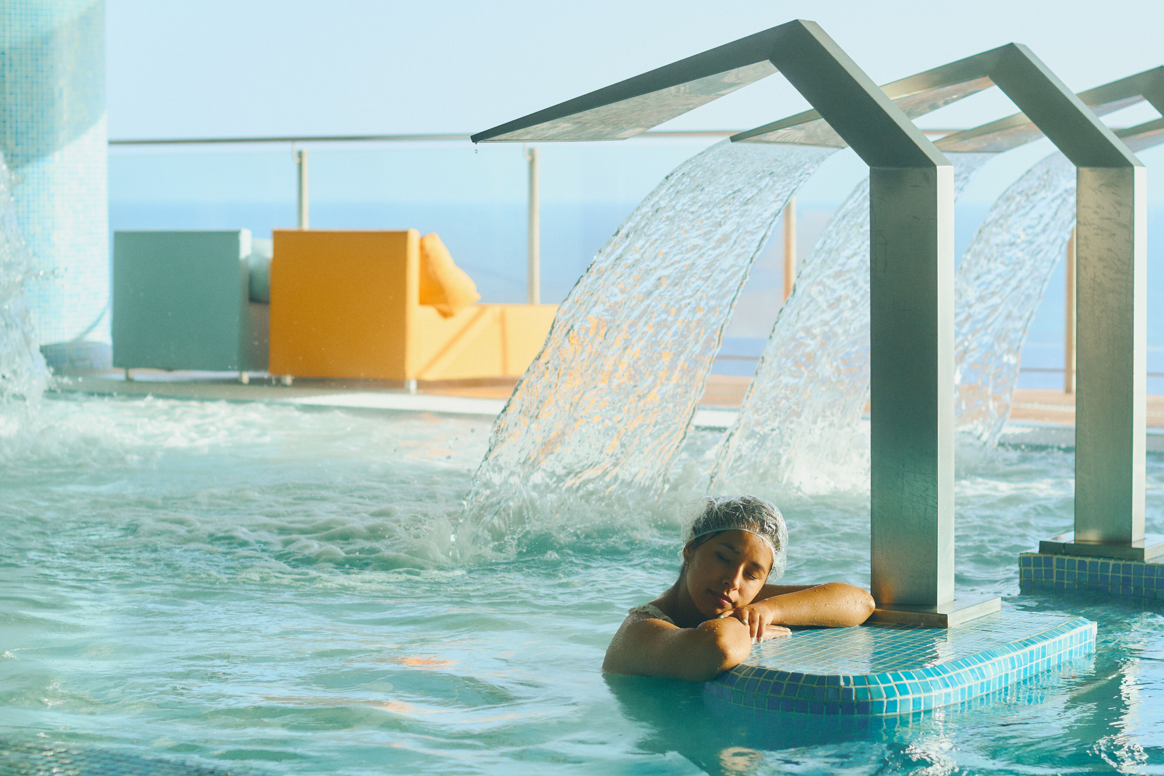 A person relaxing in a pool with water jets, surrounded by a modern architectural structure.