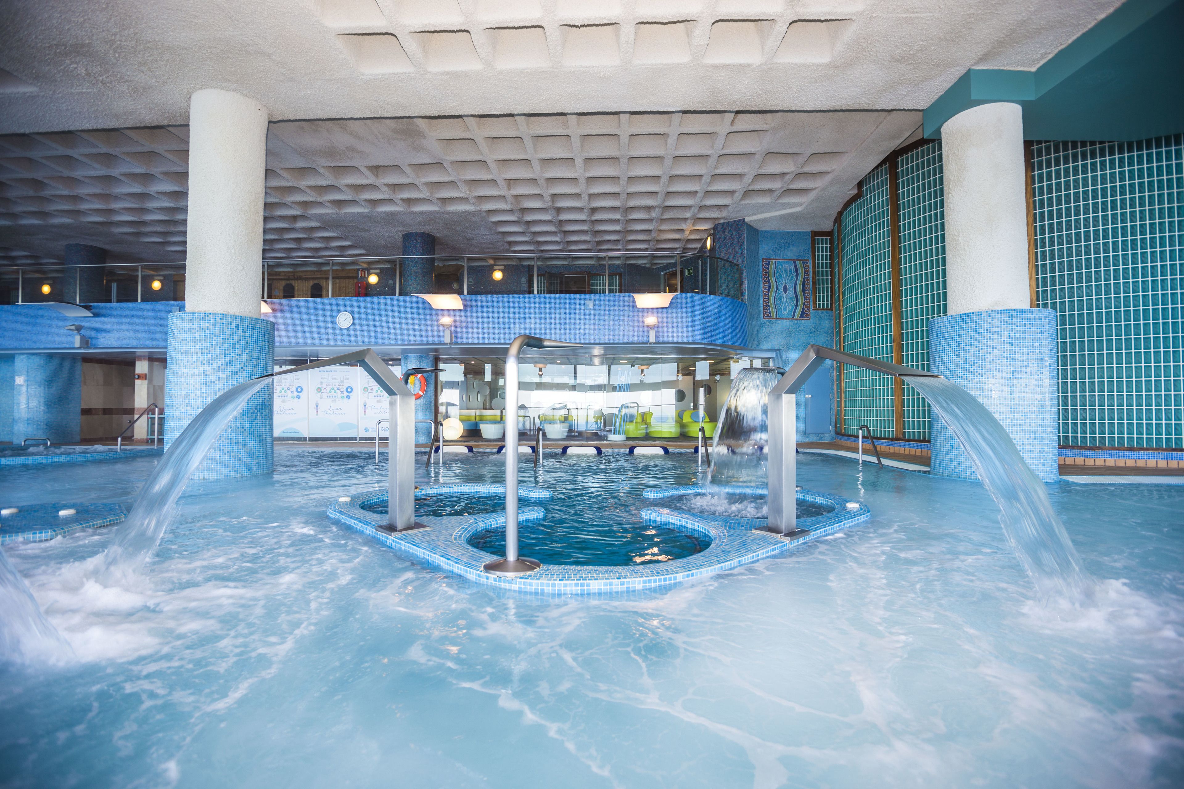 Une piscine intérieure dotée d’un élément décoratif central, de murs carrelés et d’un plafond orné d’un motif en réseau.