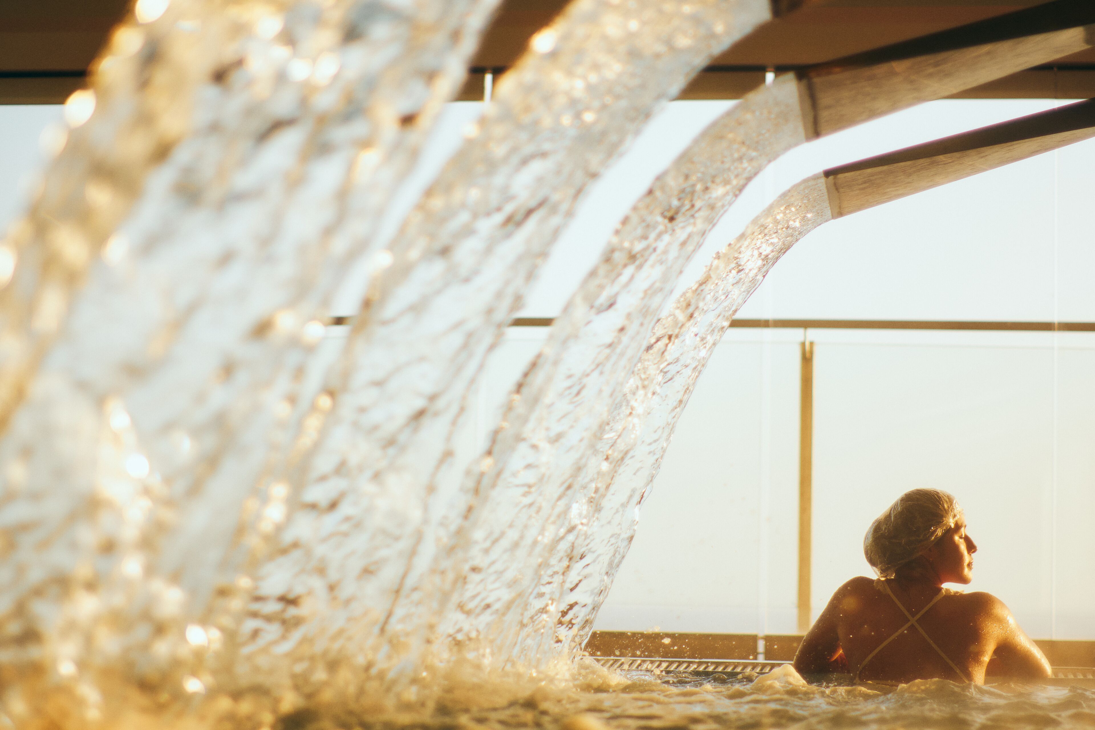 A person in a hot tub with water flowing over them, viewed from the side.