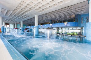 Une piscine intérieure dotée de plusieurs éléments aquatiques, notamment des fontaines et un toboggan.