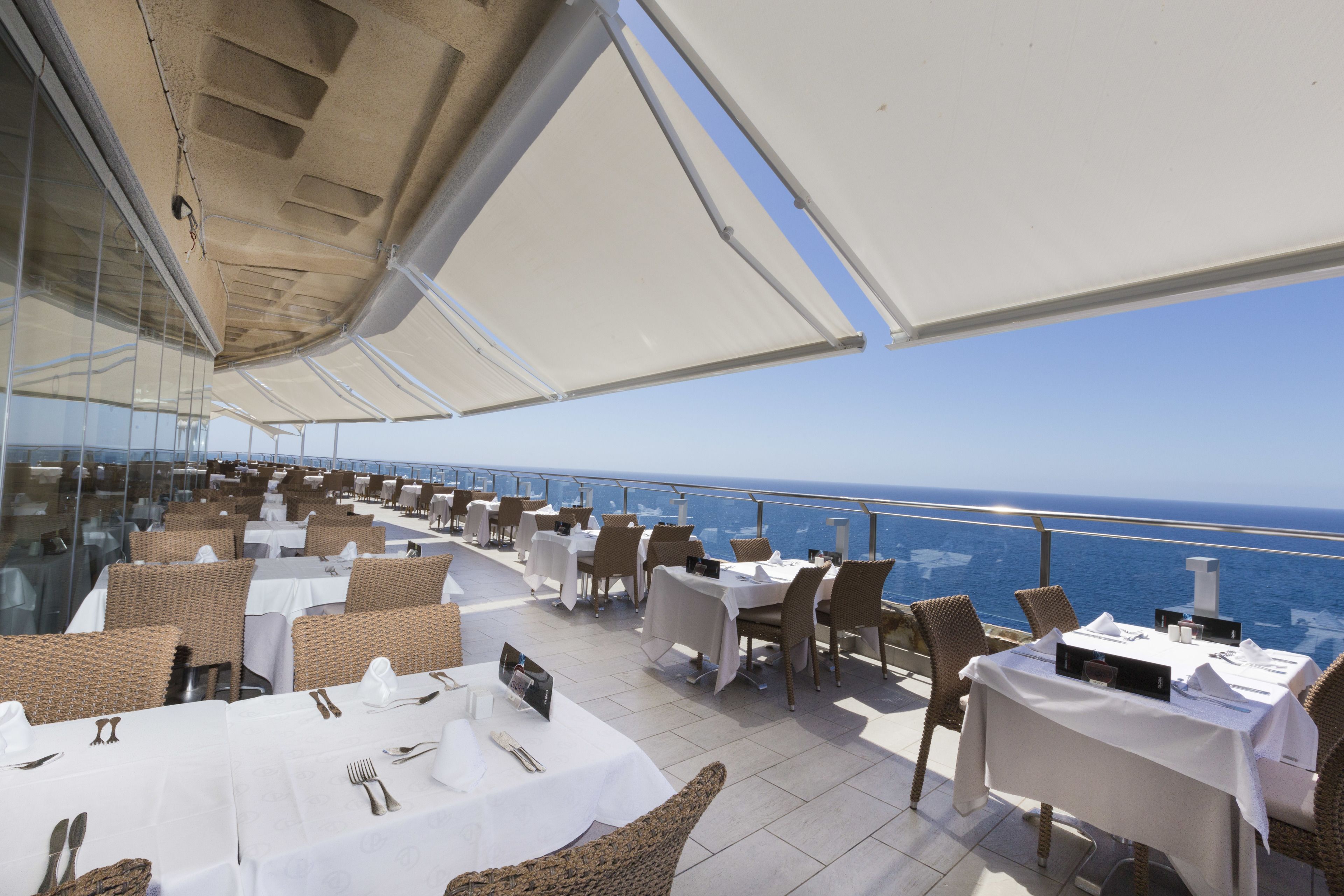 A rooftop dining area with tables and chairs, overlooking the ocean.
