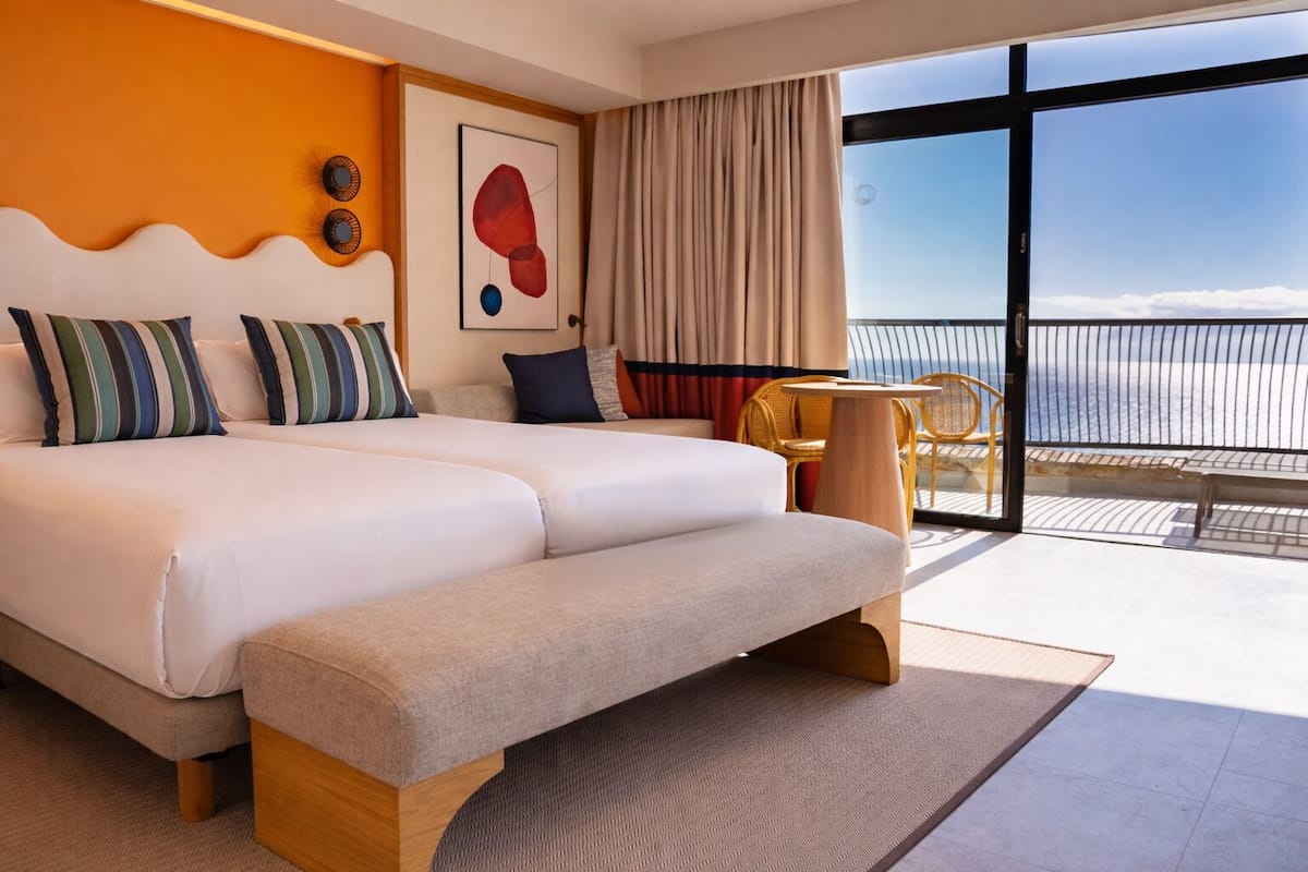 Ein Hotelzimmer mit einem großen Bett, einem kleinen Tisch, einem Sessel und Blick auf den Ozean.