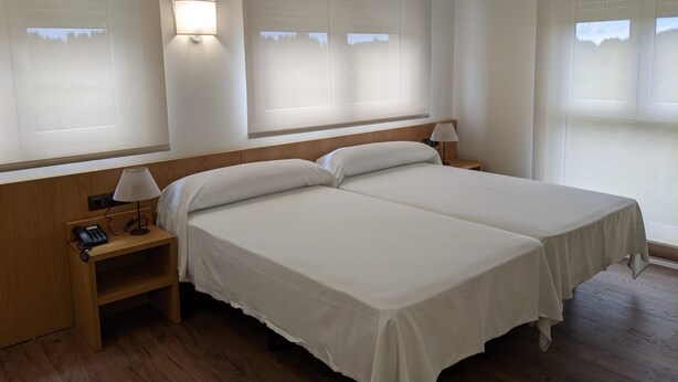 A hotel room with two single beds, a wooden nightstand with a phone, and two wall-mounted lamps. - Hotel Arias Aeropuerto (Castrillon)