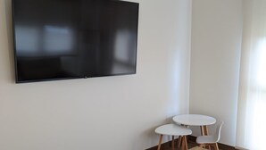 A modern living room with a flat-screen TV mounted on the wall, a wooden coffee table, two white chairs, and a sofa. - Hotel Arias Aeropuerto (Castrillon)