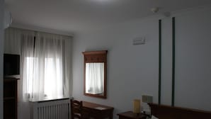 A room with a bed, a desk, a chair, a television, and a window with curtains.