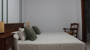 A bedroom with a bed, pillows, a wooden nightstand, a chair, and a lamp.