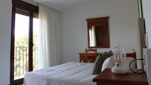 A bedroom with a bed, a wooden nightstand, a lamp, a mirror, and a window with curtains. - Hotel La Posada del Conde (Ardales)