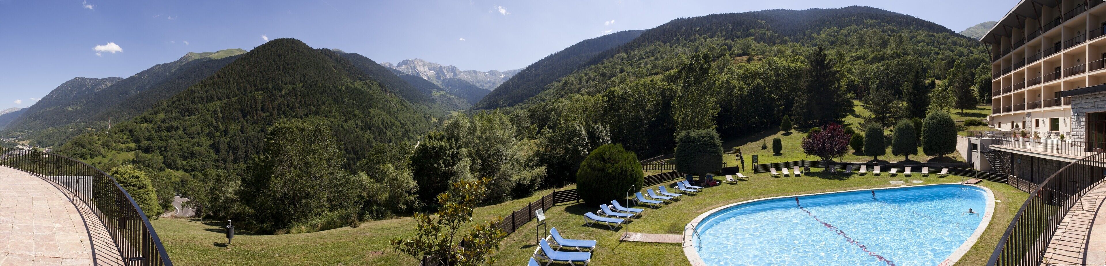 A pool area with lounge chairs, surrounded by lush greenery and mountains in the background.