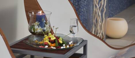 A table with a glass bowl containing fruit and a candle, a glass of water, and a candle in a vase.